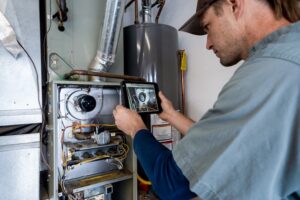 Young Male Technician Photographing a Furnace Hot Water Heater and Air Conditioning Unit Inside a Residential Home Garage